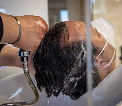 la testa di un uomo poggiata sul lavabo mentre gli viene fatto lo shampoo