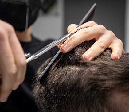 mani di un giovane parrucchiere mentre realizza un taglio maschile